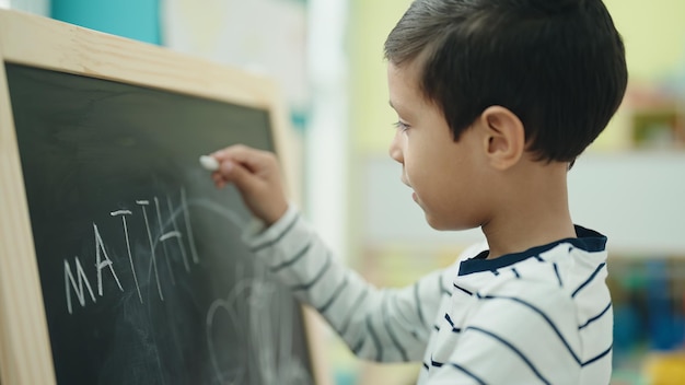 幼稚園で黒板に書いている愛らしいヒスパニックの男の子就学前の学生