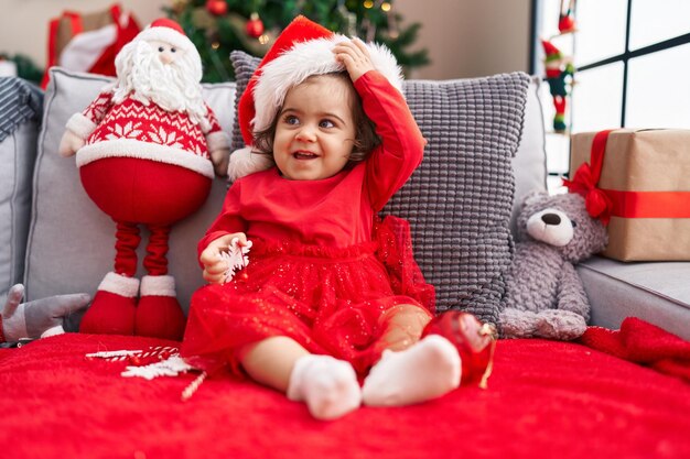 Adorable hispanic girl smiling confident sitting on sofa by christmas tree at home