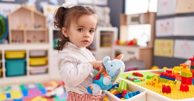 Adorable hispanic toddler holding elephant toy standing at kindergarten