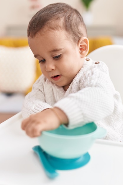 Adorable hispanic toddler sitting on highchair with relaxed expression at home