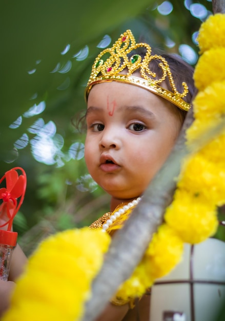 Adorable infant dressed as hindu god krishna cute facial expression playing at tree at janmashtami