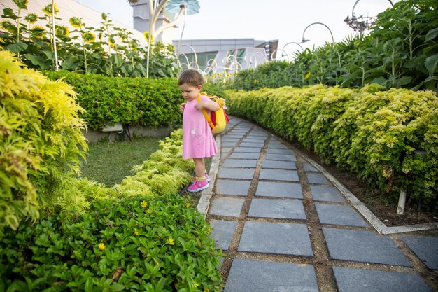 公園で赤ちゃんのバックパックスタンドとピンクのドレスで愛らしい幼児の女の子