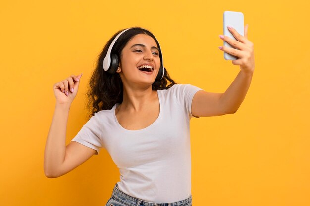 Adorable joyful young woman listening to music taking selfie