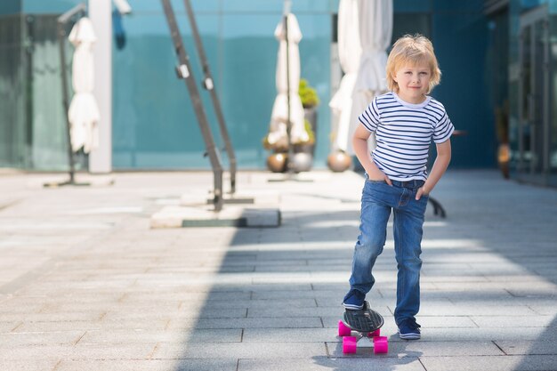 Adorable kid outdoors. Cute pretty cheerful child holding skateboard  Casual boy on summer time skating on a skateboard.