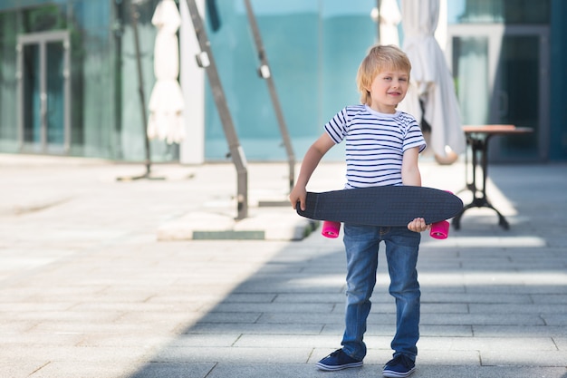 Adorabile bambino all'aperto. carino carino bambino allegro azienda skateboard casual ragazzo in estate pattinaggio su uno skateboard.