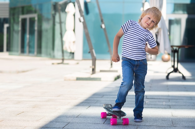 Adorable kid outdoors. Cute pretty cheerful child holding skateboard  Casual boy on summer time skating on a skateboard.