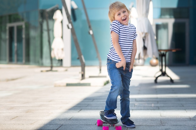 Adorable kid outdoors. Cute pretty cheerful child holding skateboard  Casual boy on summer time skating on a skateboard.