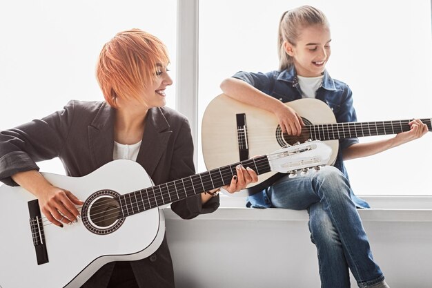 Adorable kid practicing guitar with happy female teacher