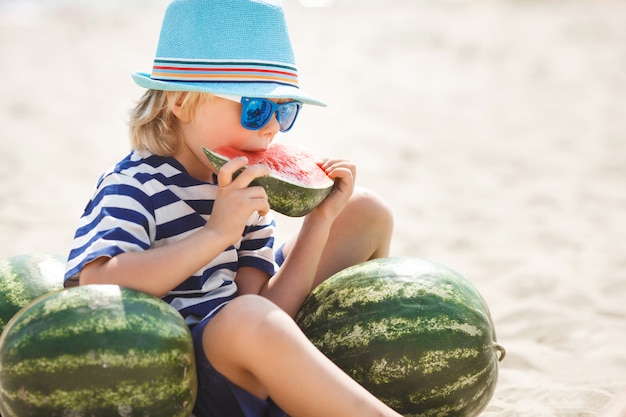 Adorable kid at the sea shore eating juicy watermelon. Cheerful child on summer time on the beach. Cute little boy outdoors