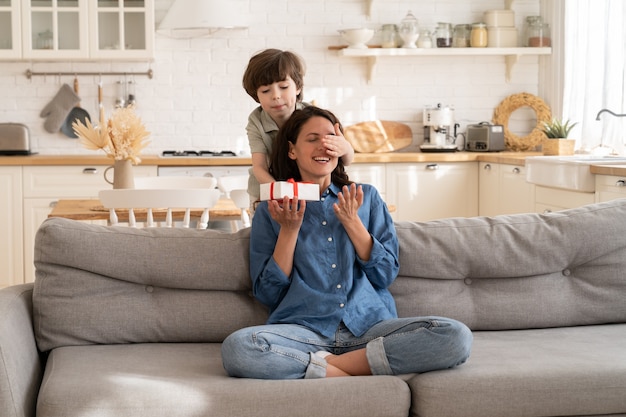 Adorable kid son greeting mom with mother day birthday with gift box closing eyes of excited mum