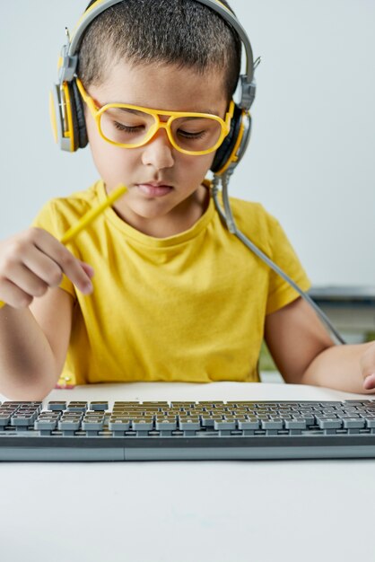 온라인 과정을 듣는 헤드폰이 달린 노란색 티셔츠를 입은 사랑스러운 아이.