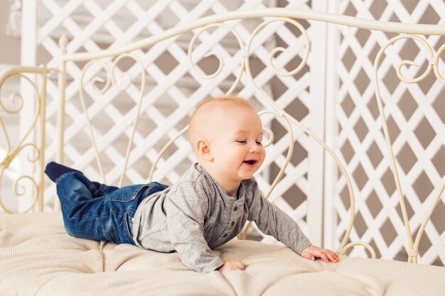 Adorable laughing baby boy in sunny bedroom