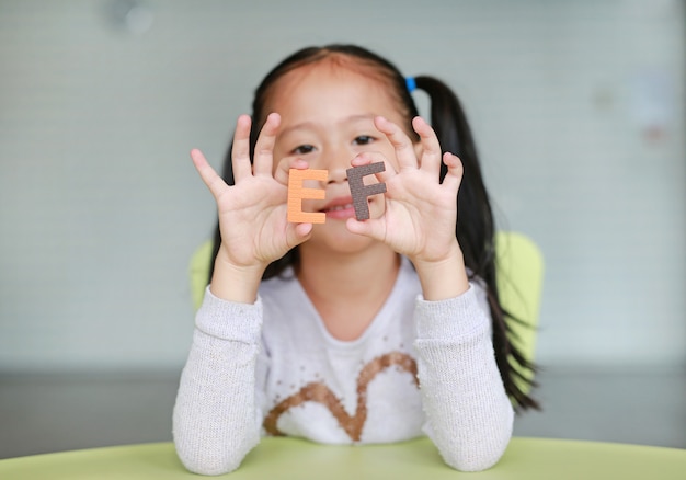 Adorable little Asian child girl holding alphabet letters on her face