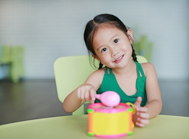 Adorable little Asian child girl play hitting toy drum in children room.