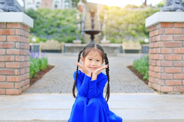 Adorable little Asian child girl sitting on stair in the garden with looking camera.