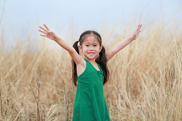 乾いた芝生のフィールドで両手を広げて愛らしい小さなアジア子供女の子。