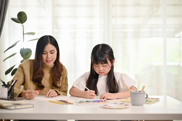 Un'adorabile bambina asiatica che si concentra sulla pittura e sul disegno con sua madre a casa