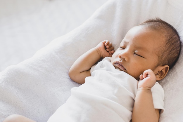 Очаровательный маленький азиатский новорожденный ребенок спит на удобной кровати