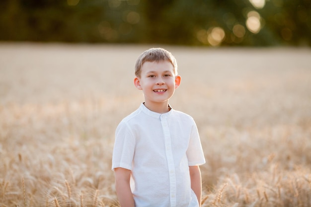 Adorable little blonde boy 8 years old in the sun at sunset in a wheat field Happy child outside Walk Warm summer Emotions