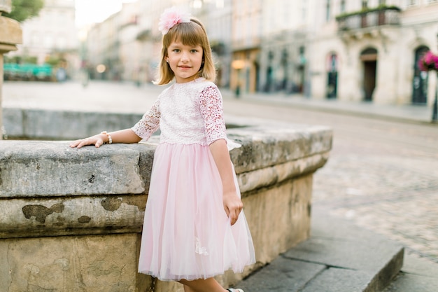 Adorable little blonde girl in a pink dress in the city