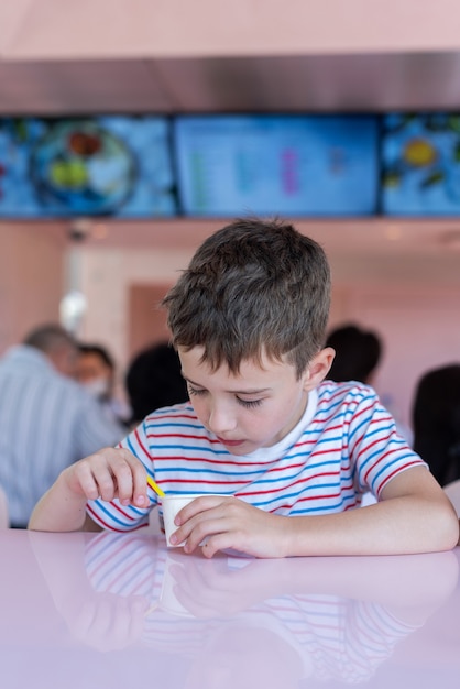 Adorable little boy eating frozen yoghurt ice cream in city cafe