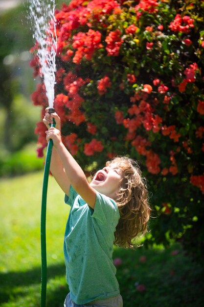 愛らしい男の子は、家の外で植物に水をやっています。自然の中の木のための子供と子供の教育のための植物成長学習活動の概念