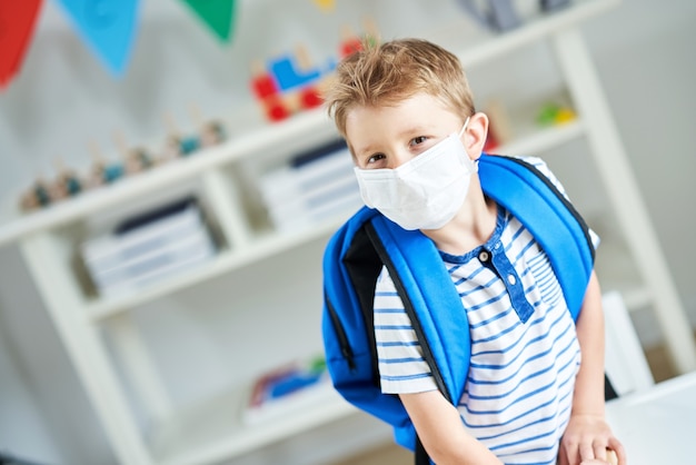 Adorable little boy in kindergarten with mask on due to coronavirus pandemic