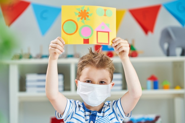 Очаровательный маленький мальчик в детском саду в маске из-за пандемии коронавируса
