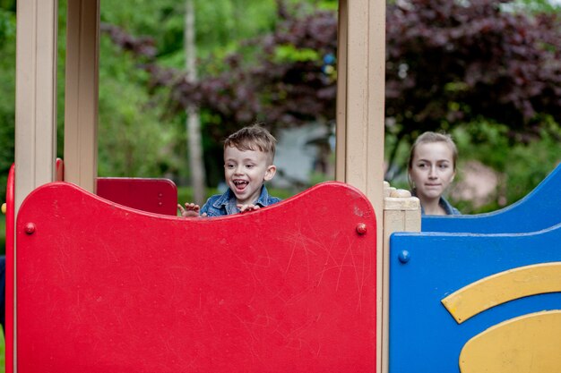 Adorabile bambino giocando su uno scivolo in un parco giochi all'aperto per bambini seduti in cima con un'espressione pittoresca mentre si prepara a scivolare giù