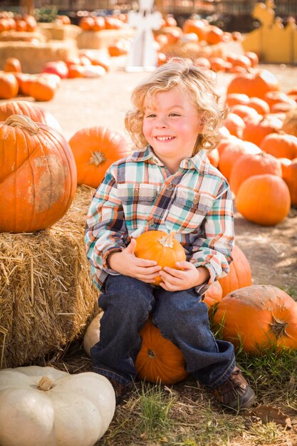 Adorable little boy sitting and holding his pumpkin in a rustic ranch setting at the pumpkin patch