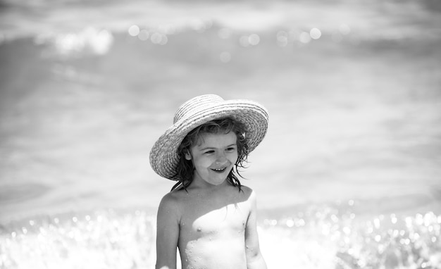 Adorable little boy in straw hat at beach during summer vacation Portrait of playful kid on the sea