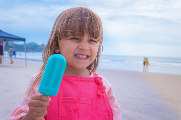 Adorable little caucasian girl with a popsicle on the beach on vacation