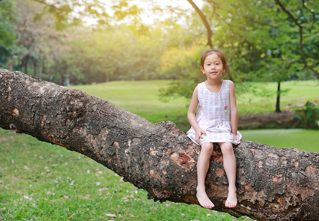 愛らしい小さな子供の女の子が登ると屋外の庭の大きな木の幹で休みます。