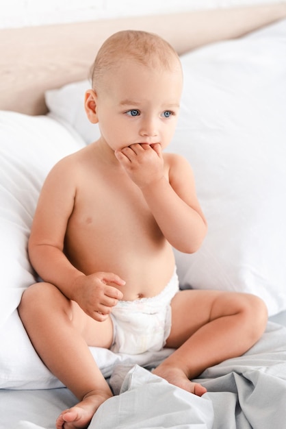 Foto adorabile bambino seduto sul letto con morbidi cuscini bianchi