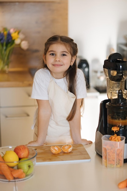 Adorable little girl in apron stand in the kitchen table full of organic vegetables and fruits