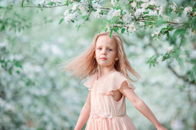 Adorable little girl in blooming cherry tree garden on spring day