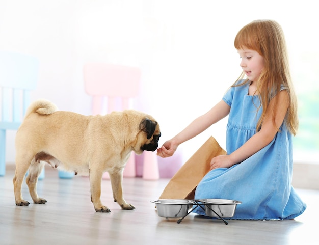 Photo adorable little girl feeding cute pug