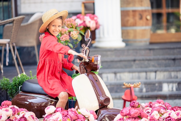 Adorable little girl in hat on the moped outdoors