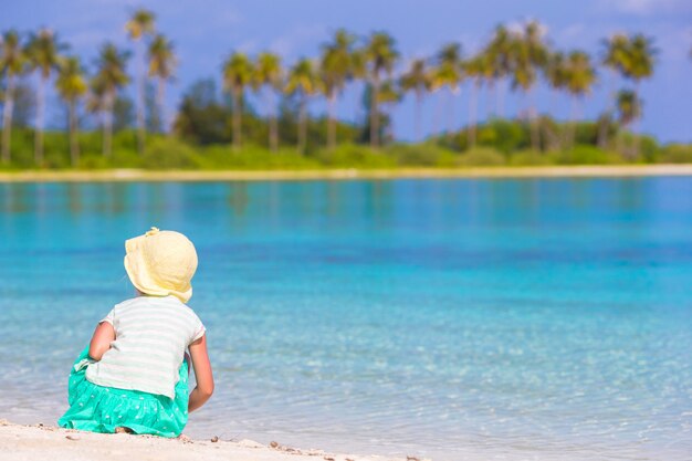 Adorable little girl in hat on white beach 