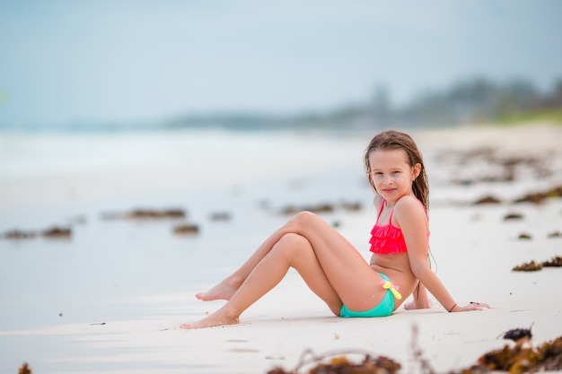 Adorable little girl have fun at shallow water on white beach