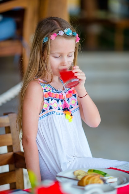 Adorable little girl having breakfast at outdoor cafe. Lid drinling fresh juice