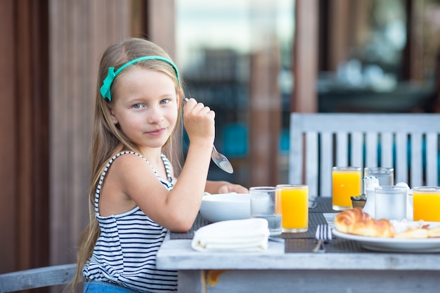 Bambina adorabile che mangia prima colazione al caffè all'aperto