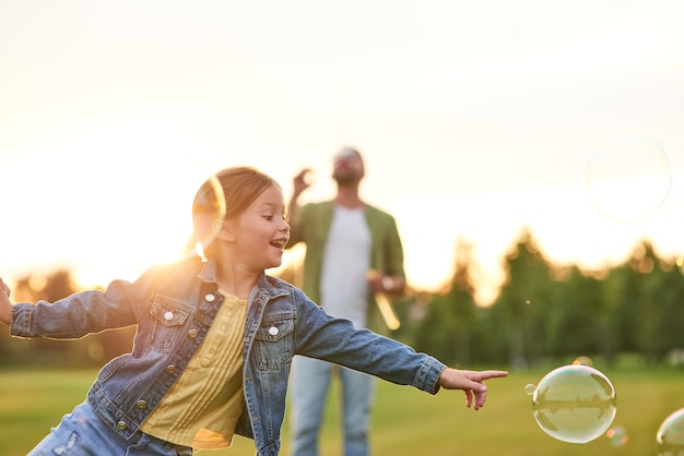 Adorable little girl having fun with soap bubbles on a sunny day daughter and dad spending time