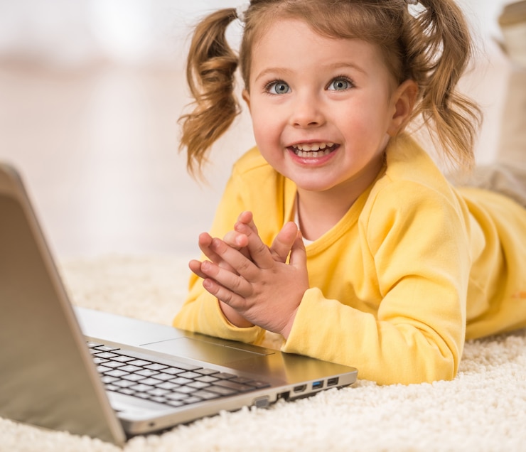 Photo adorable little girl is playing with laptop lying on floor.