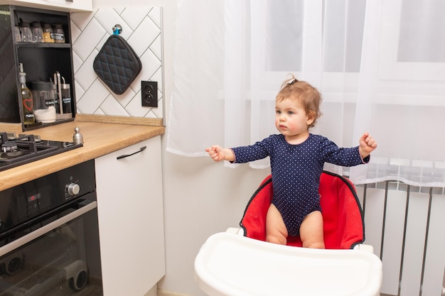 Adorable little girl is standing in a feeding chair and waiting for food