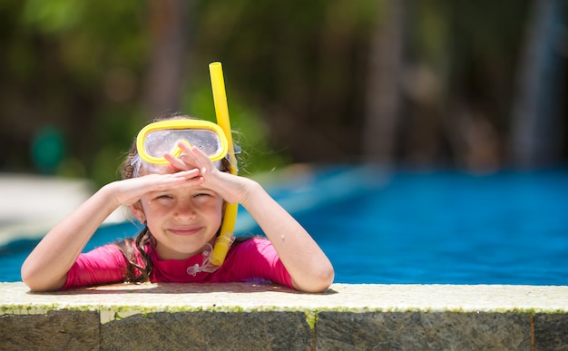 Adorable little girl at mask and goggles in swimming pool