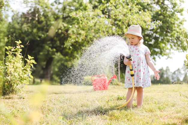 暑くて晴れた夏の日に庭のホースで遊ぶ愛らしい少女