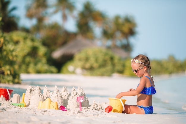 Прелестная маленькая девочка играя с игрушками пляжа во время тропических каникул