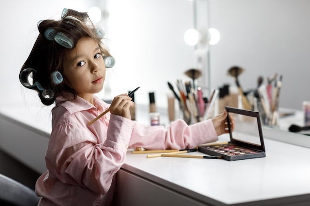 Adorabile bambina che gioca con il cosmetico di sua madre davanti allo specchio a casa