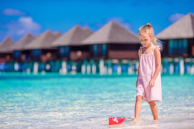 Adorable little girl playing with origami boat in turquoise sea